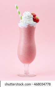 Glass of strawberry milkshake with whipped cream and fresh strawberries on pink background