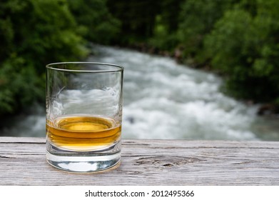 Glass of strong scotch single malt whisky with fast flowing mountain river on background, Scotland - Shutterstock ID 2012495366