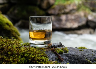 Glass of strong scotch single malt whisky with fast flowing mountain river on background, Scotland - Shutterstock ID 2013433016