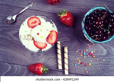 Glass Sundae With Tasty Milk Ice-cream With Sauce, Ripe Strawberries And Crispy Sweet Stick On The Wooden Table And Bowl With Cherries. Sundae Ice Cream In Cup, Top View