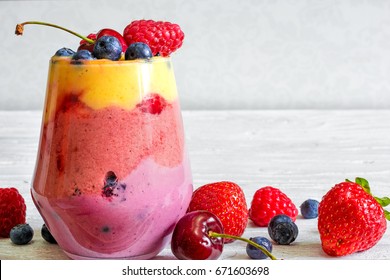 Glass Of Sweet Delicious Homemade Layered Smoothie Dessert Made From Fruits And Berries. Mango, Raspberry And Blueberry Smoothie. Close Up. Healthy Breakfast