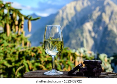 Glass of swiss or savoy dry white wine, pure chocolate with Alpine mountains peaks on background in sunny day