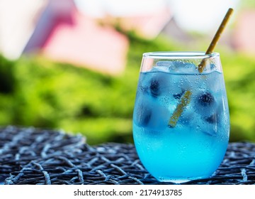 Glass of tasty blue mojito cocktail and yellow lemons on blured background. Alcohol juicy fruit blue cocktail with curacao liquor, ice cubes and blueberry in frozen glass - Shutterstock ID 2174913785