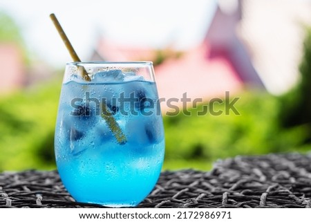 Glass of tasty blue mojito cocktail and yellow lemons on blured background.
Alcohol juicy fruit blue cocktail with curacao liquor, ice cubes and blueberry in frozen glass
