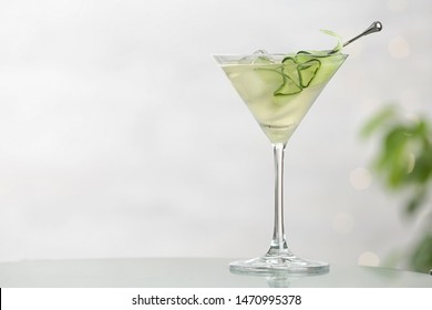 Glass of tasty cucumber martini on table against light background, space for text