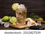 Glass of tasty ginger ale with ice cubes and ingredients on wooden table