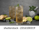 Glass of tasty ginger ale with ice cubes and ingredients on grey table