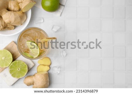 Glass of tasty ginger ale with ice cubes and ingredients on white tiled table, flat lay. Space for text