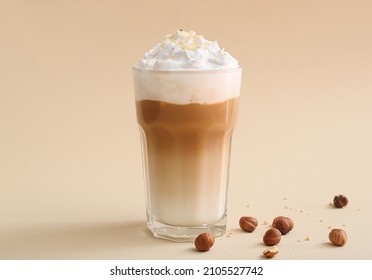 Glass of tasty latte with nuts on beige background