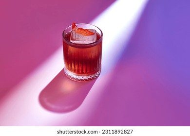 Glass of tasty Negroni cocktail with bitter flavor and ice garnished with orange peel. Served on table over night club glow. Mixed light. Copy space for text. Concept of celebration, bar, ad - Powered by Shutterstock