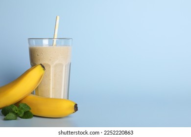 Glass of tasty smoothie with straw, bananas and mint leaves on light blue background. Space for text
