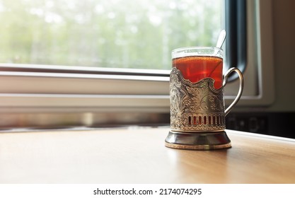 A Glass Of Tea In A Glass Holder In A Train Carriage Is On The Table In Front Of The Window.