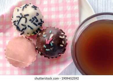 Glass With Tea And Mini Cupcakes Of Different Flavors And Colors, Seen From Above, Placed On Tray With Pink And White Checkered Paper Napkin. Tea Time Concept