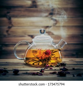 Glass teapot with blooming tea flower inside against wooden background 