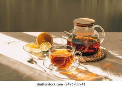 Glass teapot with brewed tea, cup of tea and lime under warm sunlight on the table, copy space - Powered by Shutterstock