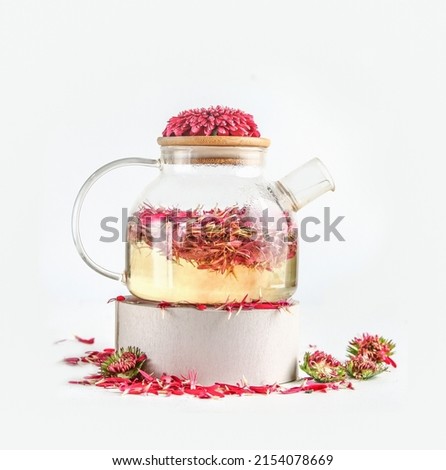Glass teapot with flowers tea with pink petals in standing on white podium at white background. Healthy lifestyle with flavored tea and edible flower. Front view. 