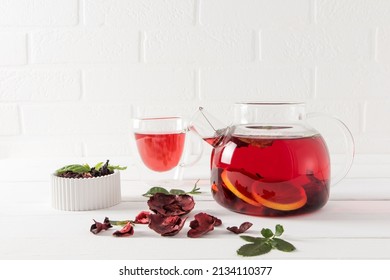 a glass teapot with freshly made hibiscus tea and lemon against a white brick wall and a cup of tea. vitamin tea for weight loss