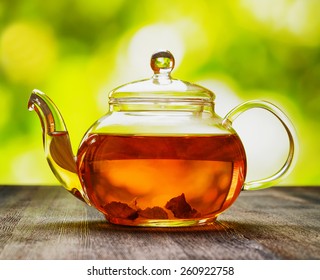 Glass teapot of invigorating fresh aromatic tea on a wooden table and on natural background.