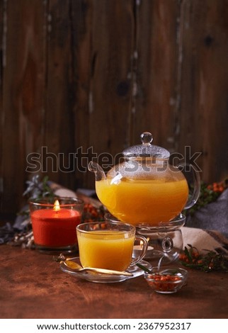 Glass teapot and sea buckthorn tea cup on wooden background. Cozy autumn composition