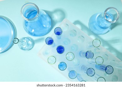 Glass test tubes and flasks with liquid on blue background, top view