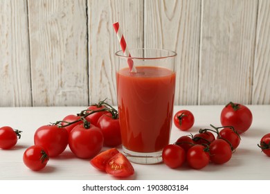 Glass with tomato juice and straw and tomatoes on wooden background