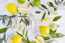 Glass Transparent Bottle Of Perfume With Lot Of Lemons, Limes, Water Drops And Green Tree Branches On The White  Marble Background. Fresh  Unisex Smell. Cooling Citrus Aroma. Perfume For Hot Weather.