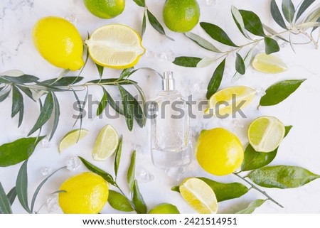 Glass transparent bottle of perfume with lot of lemons, limes, water drops and green tree branches on the white  marble background. Fresh  unisex smell. Cooling citrus aroma. Perfume for hot weather.