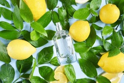 Glass Transparent Bottle Of Perfume With Lot Of Yellow Lemons, Water Drops And Green Tree Branches On The Blue Background. Fresh Summer Unisex Smell. Cooling Citrus Aroma. Perfume For Hot Weather.