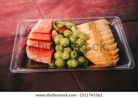 Glass tray with different fruits,watermelon,grapes,melon,kiwi, peach,on tablecloth.Natural and organic fruit platter.Melon is cut and served with the peel intact,allowing for easy,comfortable handling