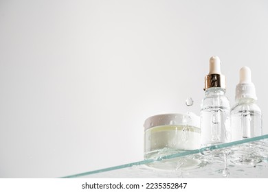 Glass tubes of cosmetic product with serum and cream on a glass shelf and water drops on a white background, bottom view. Skin care concept - Powered by Shutterstock