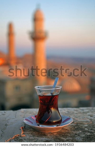 Glass of Turkish tea at sunset,\
with backdrop of historical mosque and minarets, Mardin,\
Turkey