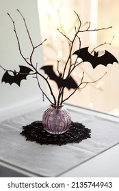 Glass Vase With Bare Branches And Black Paper Cutouts Of Bats On A Window Sill