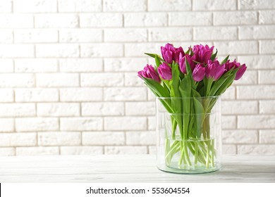 Glass vase with bouquet of beautiful tulips on brick wall background