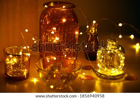 Glass vases, jars and candlesticks with led lights on a wire. Cozy details of home decor. Christmas decorations on the table.