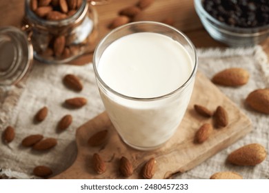 A glass of vegan almond milk on a wooden table, with whole almonds and raisins