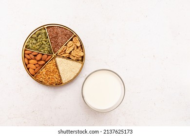 Glass of vegetable milk and a plate divided into sectors with various seeds and nuts. Concept: alternative, vegetable milk.