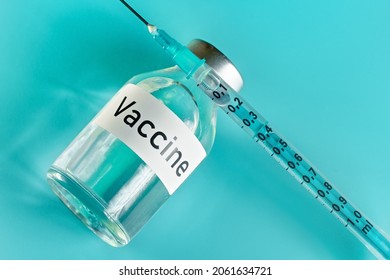 Glass Vial With Label Vaccine And Hypodermic Syringe Needle Near, View From Above On Green Cyan Background