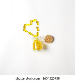 Glass Vial With Yellow Vitamins Tablets, Fish Oil, Omega Vitamin E. A Small Retro Jar With A Cork, Lies With Scattered Pills In Shape Of Heart On A White Background. Flat Lay With A Copy Space.