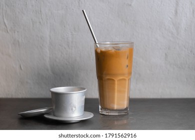 A glass of Vietnamese iced coffee with Vietnamese coffee filter in the background