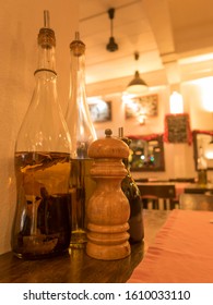 Glass Vinegar Bottles With A Wooden Pepper Grinder On A Restaurant Table With Warm Cosy Lighting