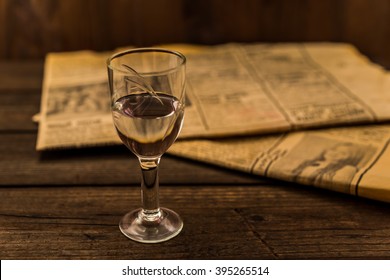 Glass Of Vodka And Newspaper On An Old Wooden Table. Angle View, Focus On The Glass Of Vodka