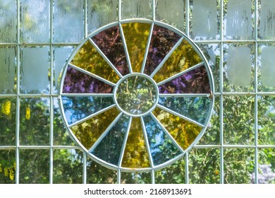 A glass wall of a greenhouse with a window of multi-colored glass