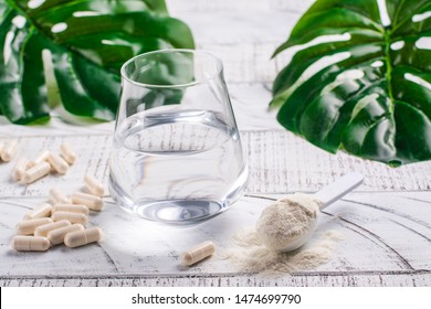 Glass of water, collagen powder and pills on white wooden table. Healthy lifestyle concept. Copy space