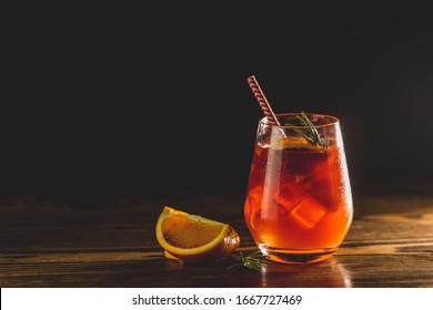 Glass With Water Drops Of Italian Aperol Spritz Cocktail With Orange Slices, Ice And Minton Dark Wooden Table With Amazing Back Light Milano Spritzer Alcoholic Cocktail With Red Bitter, Dry White Win