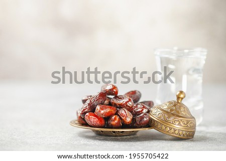 A glass of water and dry dates on saucer ready to eat for iftar time. Islamic religion and ramadan concept.