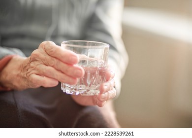 A glass of water in the hands of an old grandmother, the benefits of drinking regimen for pensioners, old age and poverty, the hands of an old woman close-up. - Shutterstock ID 2228539261