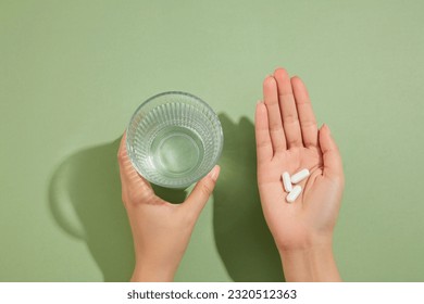 A glass of water is held in the left hand and several white pills placed on the right hand. Medication and prescription pills concept - Powered by Shutterstock