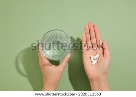 A glass of water is held in the left hand and several white pills placed on the right hand. Medication and prescription pills concept
