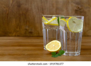 Glass Of Water With Lemon. Homemade Cold Refreshing Drink Or Water With Ice On Rustic Wood Background. Copy Space. Summer Drinks. Two Glass With Lemonade Or Mojito Cocktail With Lemon And Mint.