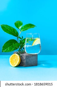 A glass of water with lemon and mint on pedestal in fashion trendy style on a blue background. Modern still life with copy space.